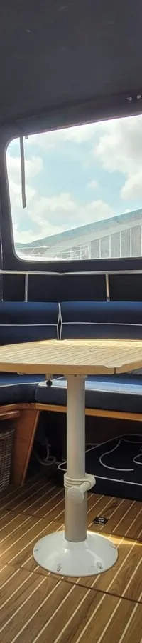 Een interieur van een boot met een U-vormige zitbank met blauwe kussens, een houten tafel en een houten vloer. — Agder 840 OK