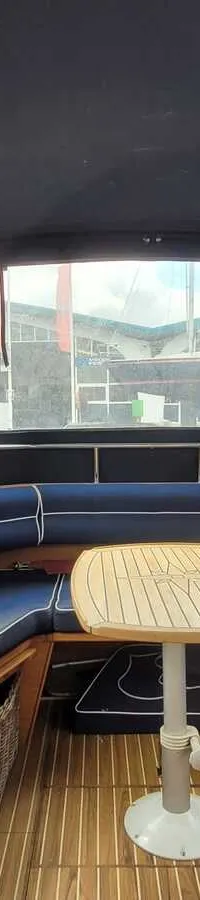 Een bootinterieur met een U-vormige blauwe bank met witte biezen, een houten tafel en een teakhouten vloer.
