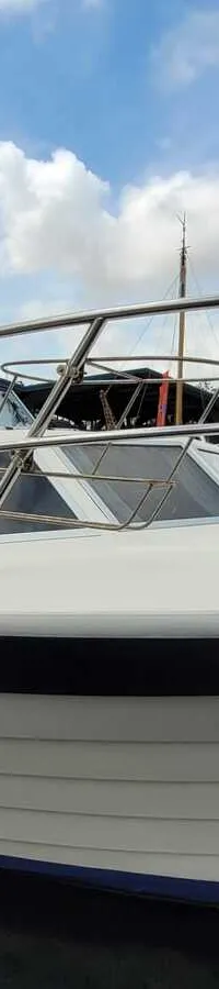Een witte motorboot met een blauwe streep en een blauw dekzeil ligt afgemeerd aan een houten steiger. — Agder 840 OK