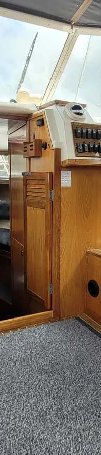 Een interieur van een boot met een stuurstand, blauwe bekleding, houten afwerking en een koelkast. — Agder 840 OK