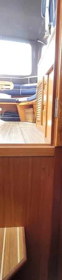 Een interieur van een boot met houten panelen, een koelkast, een zithoek met blauwe kussens en een bed. — Agder 840 OK