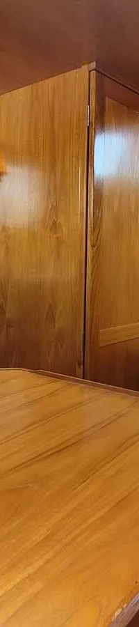 Een interieur van een boot met houten wanden en plafonds, blauwe kussens en een houten tafel op de voorgrond. — Agder 840 OK