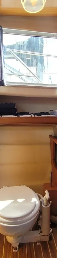 Een houten interieur met een toilet, een wastafel met kraan en een spiegel, verlicht door daglicht en lampen.
