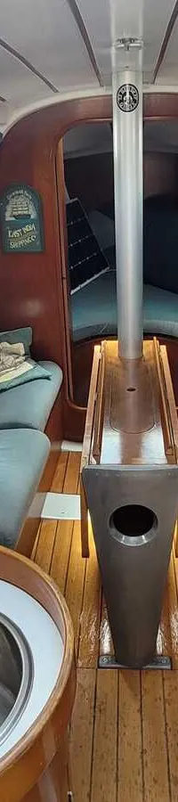 Een interieur van een boot met een kombuis aan de linkerkant en twee banken aan weerszijden van een centrale mast.