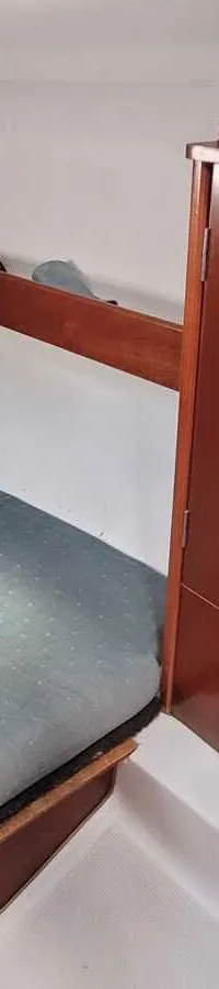 De foto toont een kajuit met een bed met een groen matras en een houten kast. — Beneteau First 310