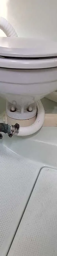 Een wit scheepstoilet met een handpomp en slangen is gemonteerd in een witte, kunststof ruimte.