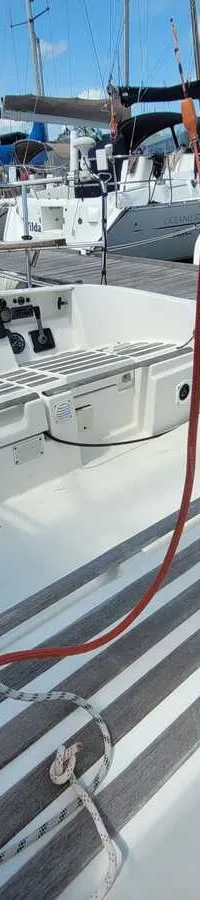 Een witte boot met grijze antislipstrips op het dek, touwen en blokken, en andere boten in een haven op de achtergrond.