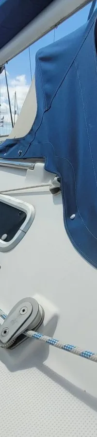 Een witte zeilboot ligt in een haven met andere boten, onder een blauwe hemel met witte wolken. — Beneteau First 310
