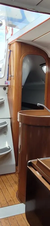 De foto toont het interieur van een boot met houten afwerking, een kombuis, zitbanken en een trap naar de kuip.