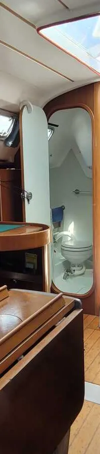 De foto toont het interieur van een boot met houten afwerking, zitbanken, een tafel, een kombuis en een toiletruimte.