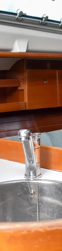 Een interieur van een boot met een rvs-gootsteen, kraan, houten kasten, een bank met kussens en patrijspoorten.