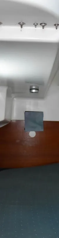 De foto toont een kajuit met een bed met blauwe matrassen, houten wanden en een wit plafond met een patrijspoort.