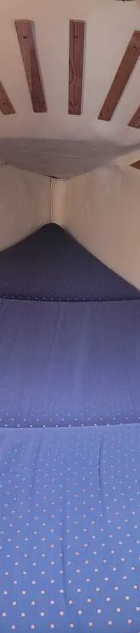 De foto toont een kajuit met een blauw matras met oranje stippen en houten latten aan het plafond en de zijkanten.