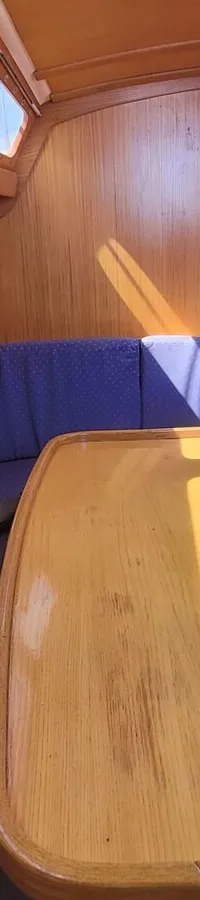 De foto toont het interieur van een boot met houten afwerking, blauwe kussens en een houten tafel in het midden.