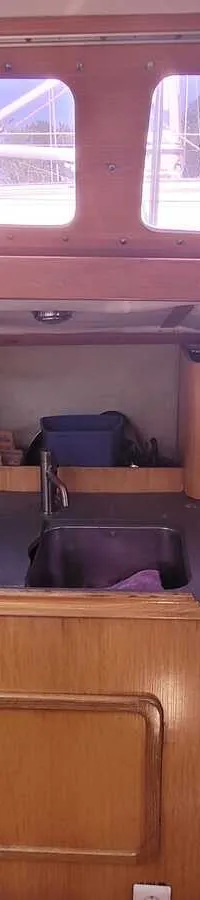 Een houten scheepsinterieur met een kombuis, inclusief een gootsteen, gasfornuis, magnetron en opbergkasten.