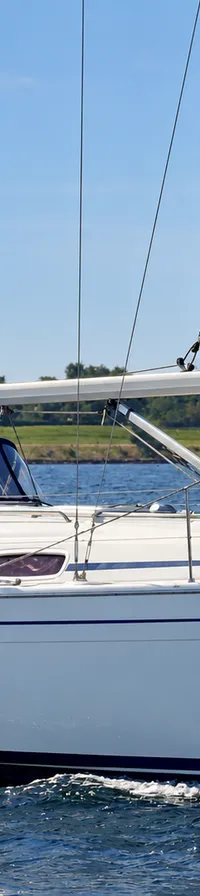 Een witte zeilboot met blauwe strepen en een blauwe buiskap vaart op het water, met een man in een blauw overhemd aan boord.