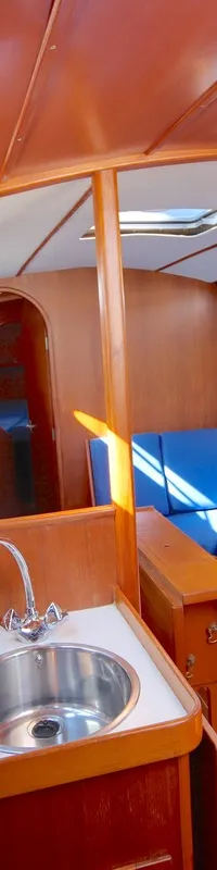 De kajuit van een boot met houten wanden en plafond, een witte aanrecht met een ronde spoelbak en blauwe kussens. — Luffe 46