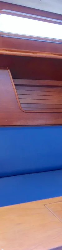 De foto toont een houten kajuitinterieur met een lange blauwe bank, een houten tafel en ramen bovenin.