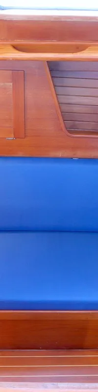 Een kajuit met houten lambrisering en een blauwe bank, met een gootsteen en kraan links en een leeslampje rechts. — Luffe 46