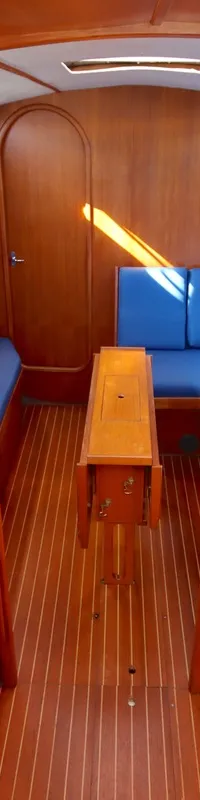De foto toont het interieur van een boot met houten afwerking, blauwe kussens, een kombuis en een tafel. — Luffe 46