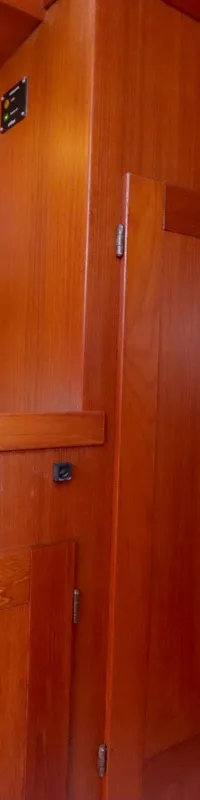 Een houten interieur van een boot met een wasbak en kraan, kasten en een doorgang naar een slaapgedeelte met een blauw…