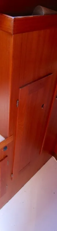 Een houten interieur van een boot met een wasbak, kraan en een doorkijk naar een slaapgedeelte met blauwe kussens. — Luffe 46