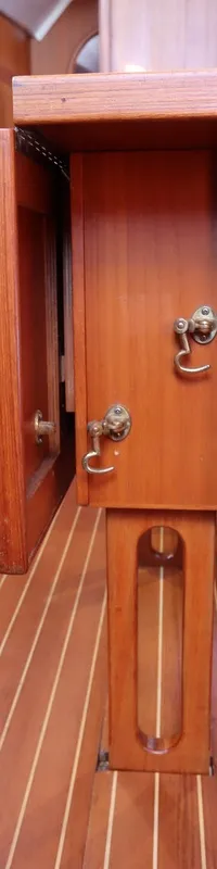 De foto toont een kajuitinterieur met een houten vloer, twee blauwe banken en een houten tafel in het midden.