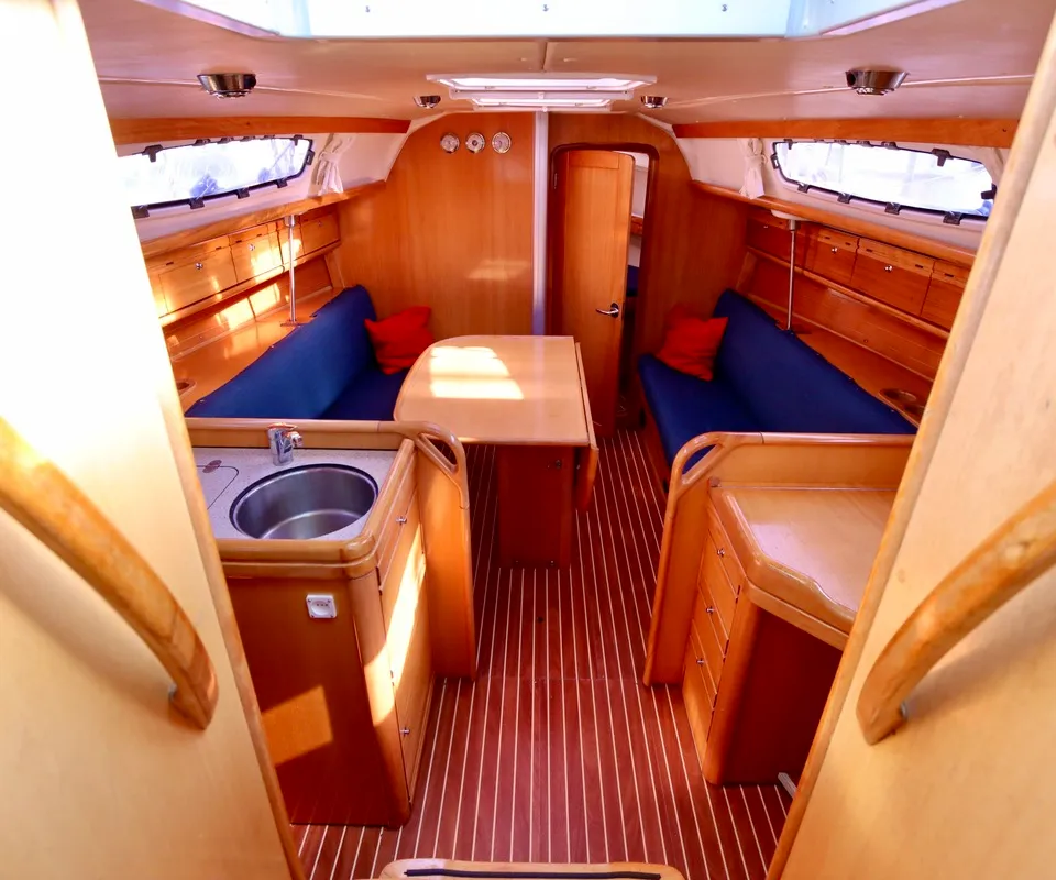 De kajuit van een boot met houten interieur, blauwe banken, een tafel en een gootsteen. — Bavaria 31