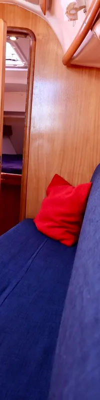 De foto toont het interieur van een boot met houten wanden, blauwe banken, een inklapbare tafel en een open deur.