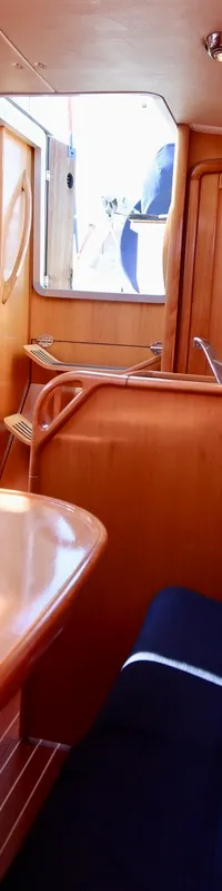 De foto toont het interieur van een boot met houten afwerking, blauwe kussens, een tafel en een kombuis. — Bavaria 31