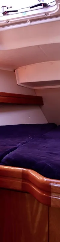 De foto toont een kajuit met een V-vormig bed met twee paarse matrassen, houten afwerking en een dakluik. — Bavaria 31
