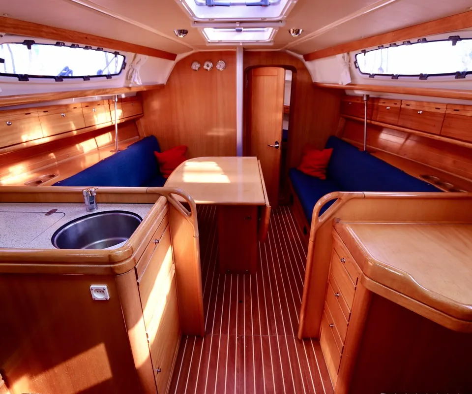 De foto toont het interieur van een boot met houten afwerking, blauwe banken, een tafel en een kombuis met spoelbak.