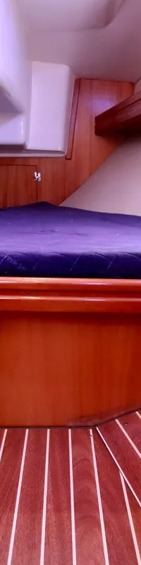 De foto toont een kajuit met een houten interieur, een donkerblauw matras en een gestreepte houten vloer. — Bavaria 31