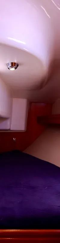 Een kajuit met een donkerblauw bed, houten kasten en een klein raam. — Bavaria 31