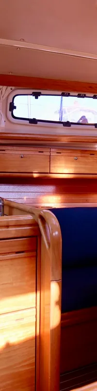 De foto toont het interieur van een boot met een houten afwerking, een kombuis, een zithoek en patrijspoorten. — Bavaria 31