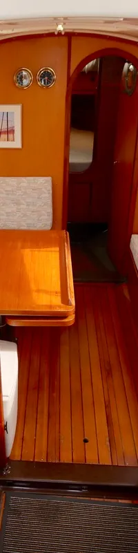 De bootkajuit toont een houten interieur met twee banken, een tafel, een kombuis met spoelbak en een doorgang naar voren.