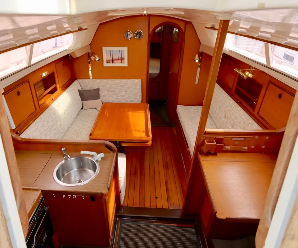 De bootkajuit toont een houten interieur met twee banken, een tafel, een kombuis met spoelbak en een doorgang naar voren.