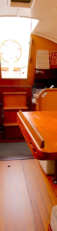 De kajuit van een boot met houten interieur, twee banken met kussens, een tafel en een kaart aan de wand. — Dehler Optima 98