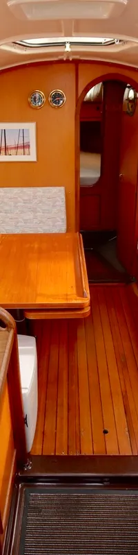 De kajuit toont een houten interieur met zitbanken, een tafel, een kombuis met spoelbak en een navigatiehoek.