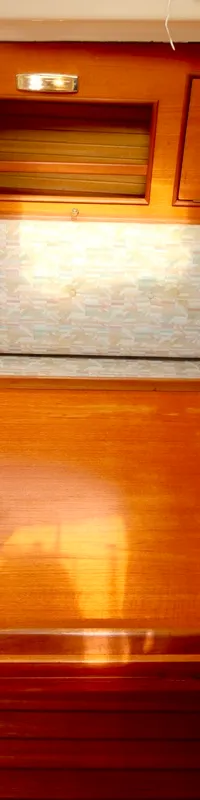Een houten interieur van een bootkajuit met een zithoek, een houten tafel, kussens met patroon en een gootsteen.