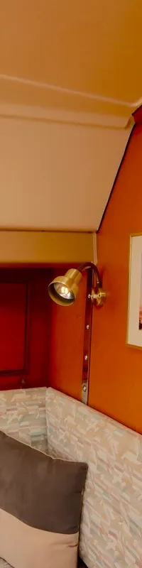 De kajuit toont houten wanden met ingebouwde kasten, een raam met gordijn, een lamp, twee instrumenten en een schilderij.