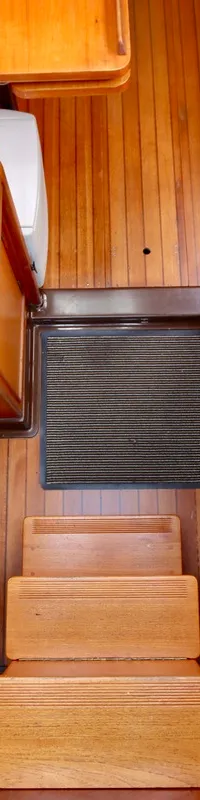 De foto toont het houten interieur van een boot met een rvs spoelbak, kookplaat, houten treden en gestreepte kussens.