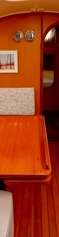 De kajuit van een boot is zichtbaar, met een houten interieur, een tafel en zitbanken met lichtgekleurde kussens.