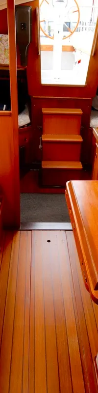 De kajuit van een boot toont een houten interieur met twee gestoffeerde banken, een houten tafel en een trapje naar voren.