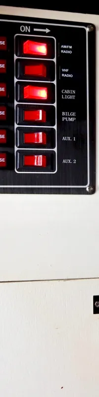 Een detailfoto van een wit bedieningspaneel met drie zwarte panelen vol rode schakelaars en zekeringen, en twee rode…