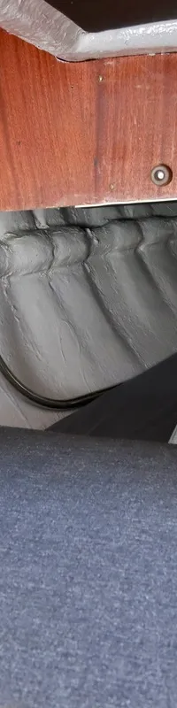 Een interieur van een boot met een schakelpaneel, houten afwerking, een grijs kussen en een opgevouwen ladder.