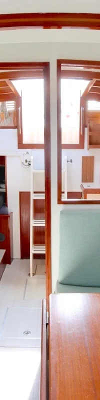 De foto toont het interieur van een boot met twee banken met lichtgroene kussens, een houten tafel en houten accenten.