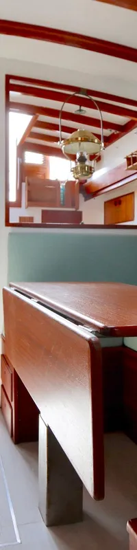 De foto toont het interieur van een boot met een houten tafel, lichtblauwe kussens en houten afwerking.