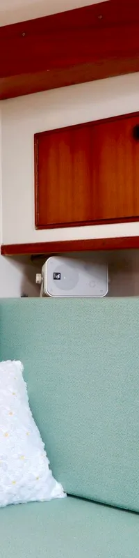 Een interieur van een boot met een mintgroene bank, een wit kussen, houten kasten en een barometer aan de muur.