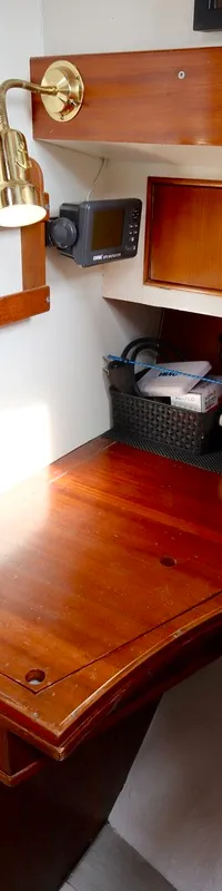 Een houten bureau met daarboven een marifoon, een dieptemeter, een lamp en opbergvakken.